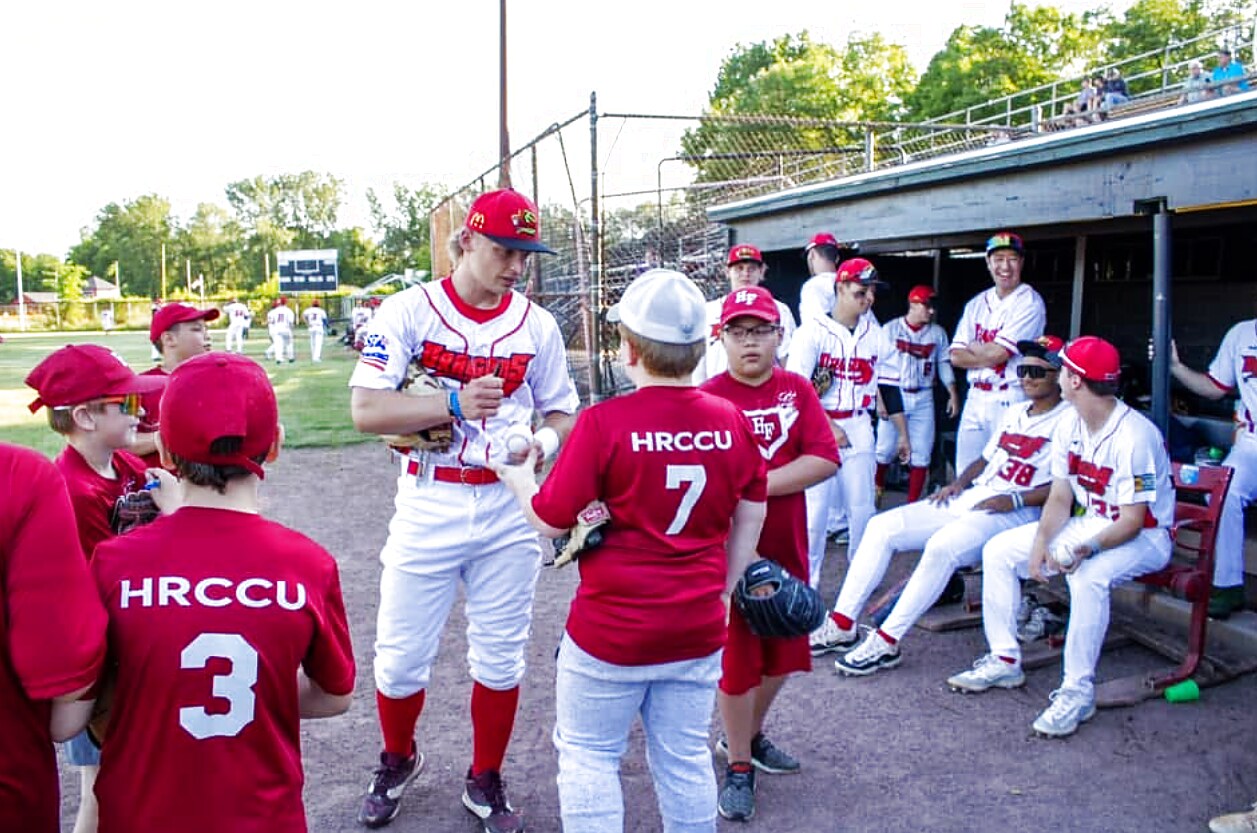 A Dragons player signing autographs for a little-league team by the dugout.