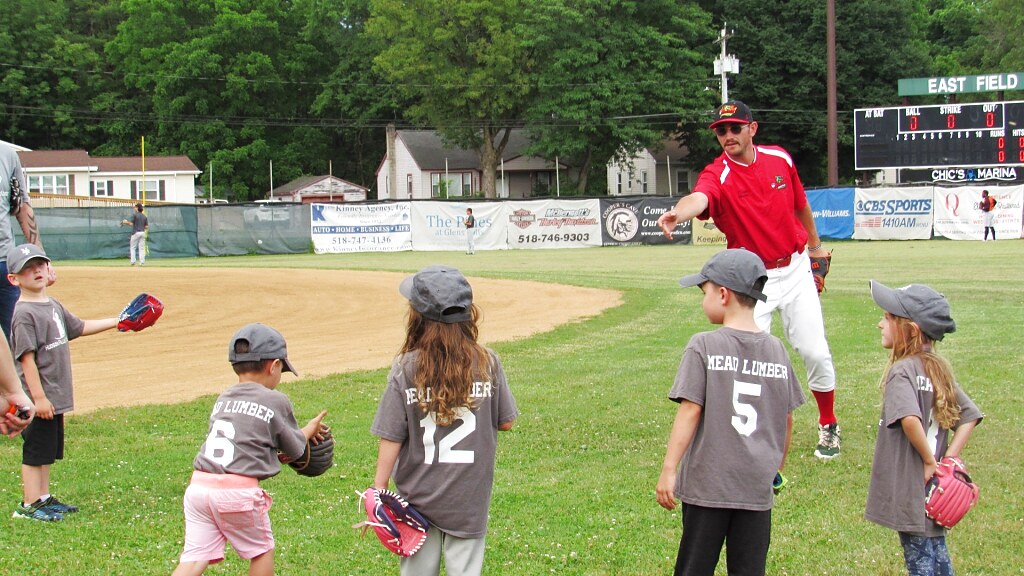 A Glens Falls Dragons player playing catch with a youth team on the grass at East Field